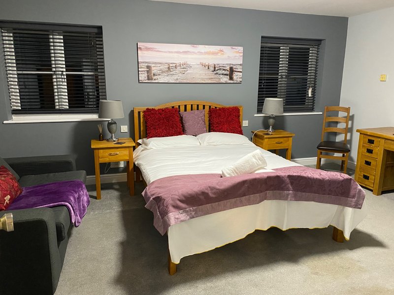 Bedroom with double bed, wooden furniture, red and purple bedding, and shuttered windows