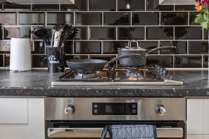 Modern kitchen with black subway tile backsplash, dark countertop, stainless steel oven, and cookware display