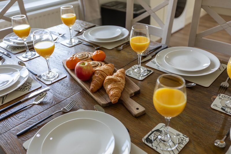 Dining table set for breakfast with orange juice, croissants, fresh fruit and place settings