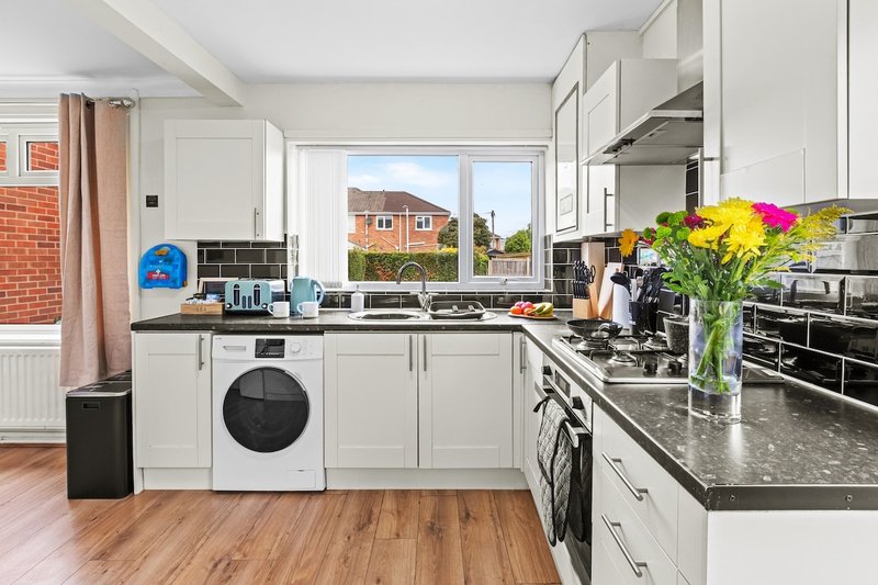 Modern kitchen with white cabinetry, black countertops, stainless steel appliances and colorful flowers in vase