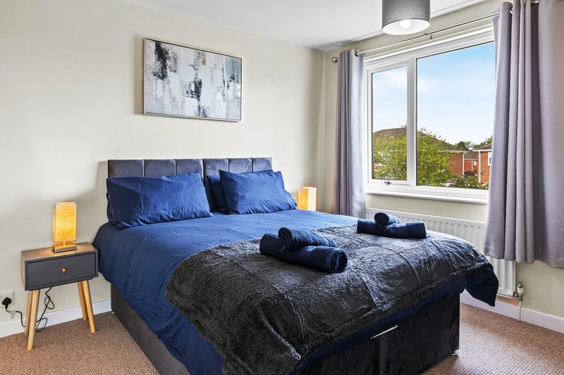 Bright bedroom with blue bedding, wooden nightstand, framed wall art and garden view