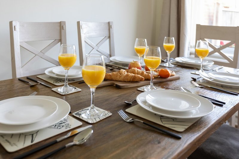 Dining table set for meal with place settings, glasses of orange juice, and fresh bread