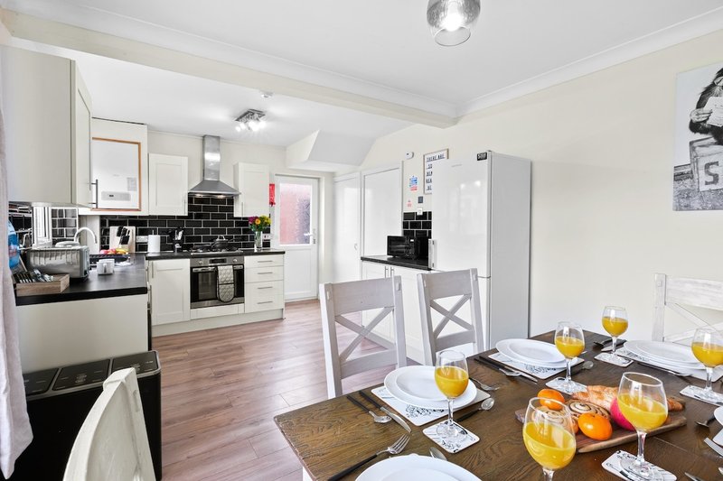Open-plan kitchen and dining area with white cabinetry, black splashback, wooden dining table and place settings