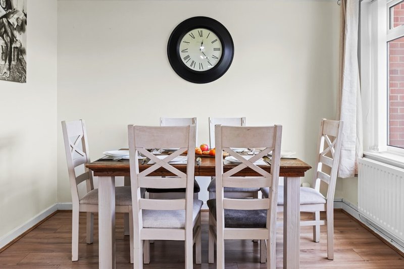 Dining room with wooden table, white chairs, wall clock and window