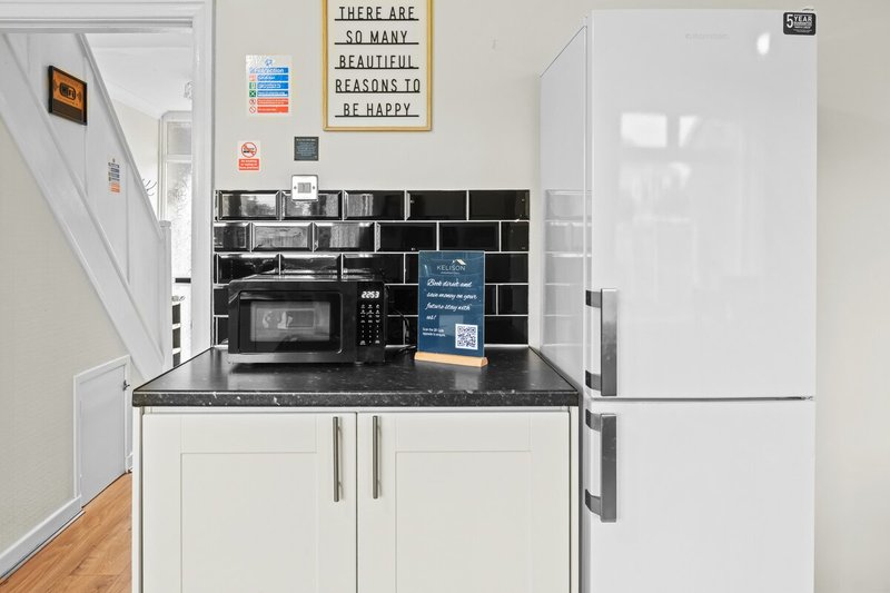 Modern kitchenette with white cabinetry, black tile backsplash, microwave and stainless steel refrigerator