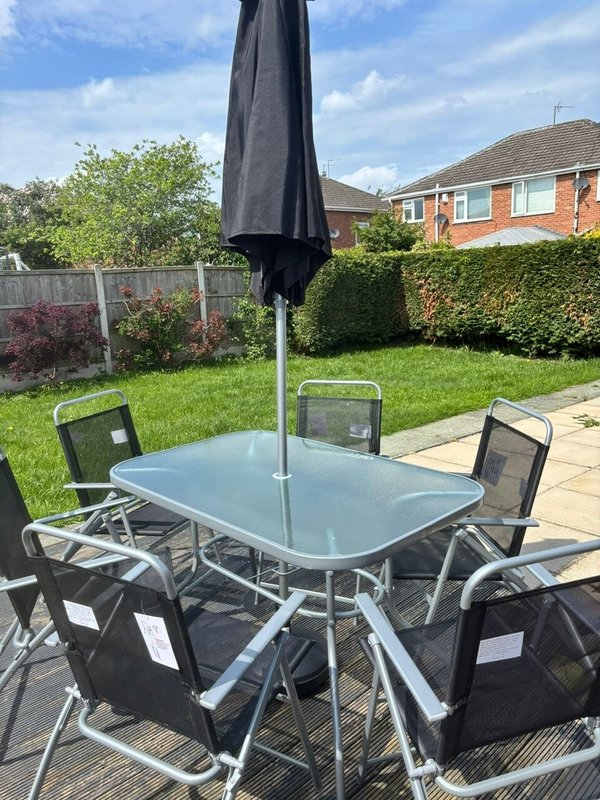 Garden patio with dining table, four chairs, umbrella and manicured lawn