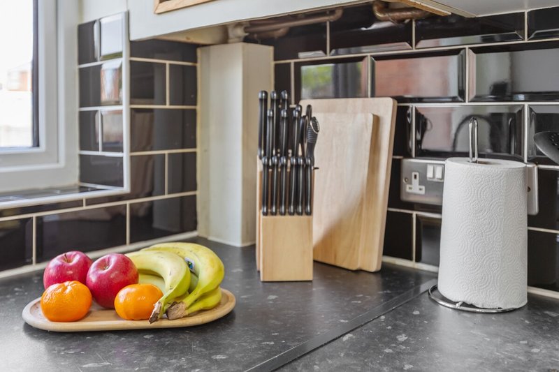 Modern kitchen with dark countertop, open shelving, fruit bowl, knife block and appliances