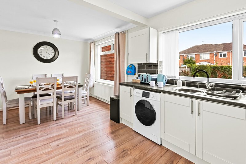 Open-plan kitchen and dining area with white cabinetry, dining table, wooden flooring and large windows