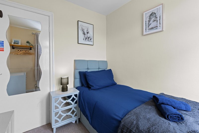 Bedroom with single bed, blue bedding, white bedside table and framed wall art