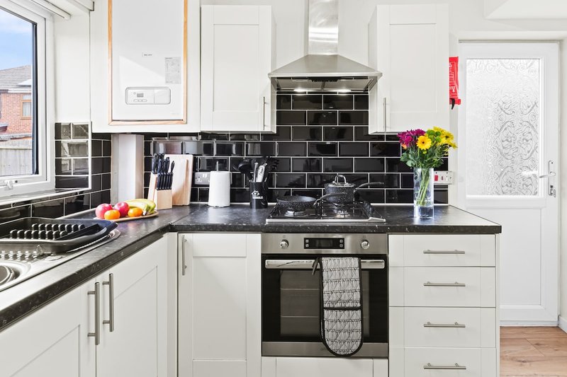 Modern kitchen with white cabinetry, black tile backsplash, stainless steel appliances and flowers
