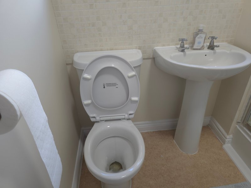Clean bathroom with toilet, pedestal sink, and tiled walls
