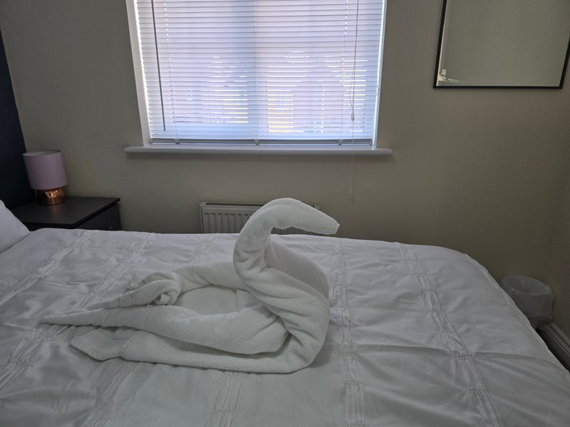 Bedroom with double bed, white bedding, window with blinds, radiator and bedside table