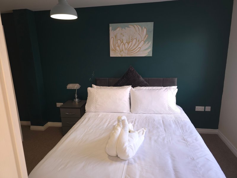 Bedroom with dark teal walls, double bed with white bedding, black headboard, and pendant light