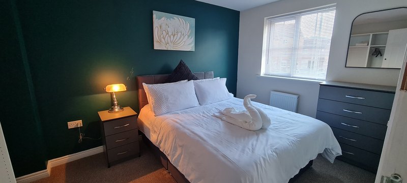Modern bedroom with double bed, teal accent wall, bedside lamp and dark furniture