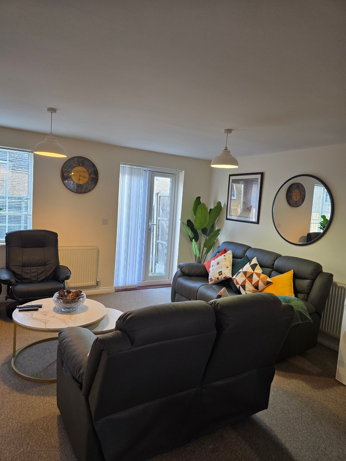 Living room with black leather sofas, round mirror, wall clock, pendant lights and glass doors