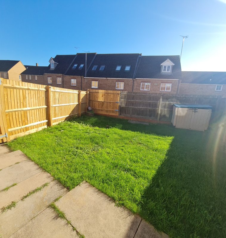Rear garden with lawn, wooden fencing, paved patio, and brick terraced houses beyond