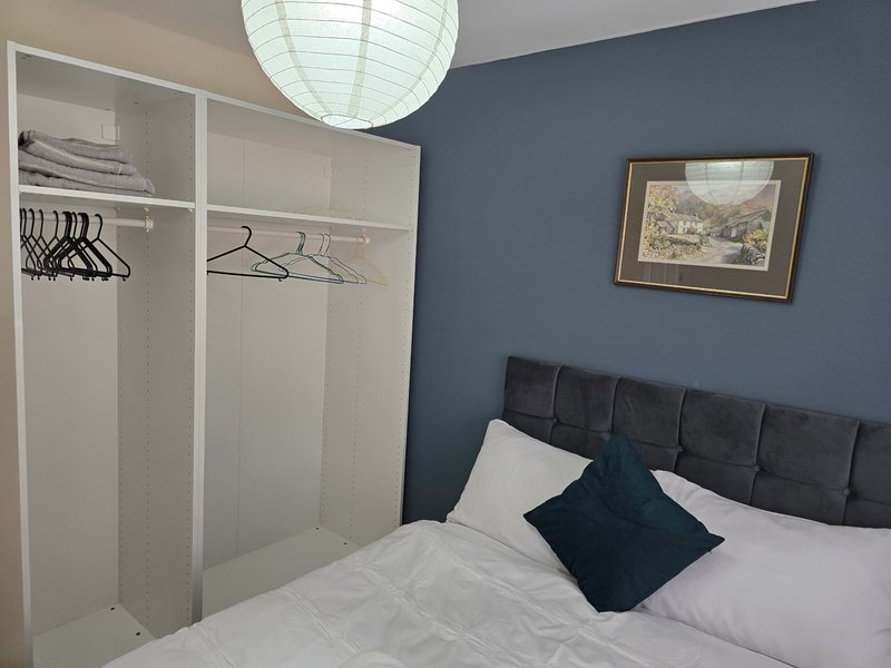 Bedroom with double bed, dark headboard, wardrobe, pendant light and framed artwork