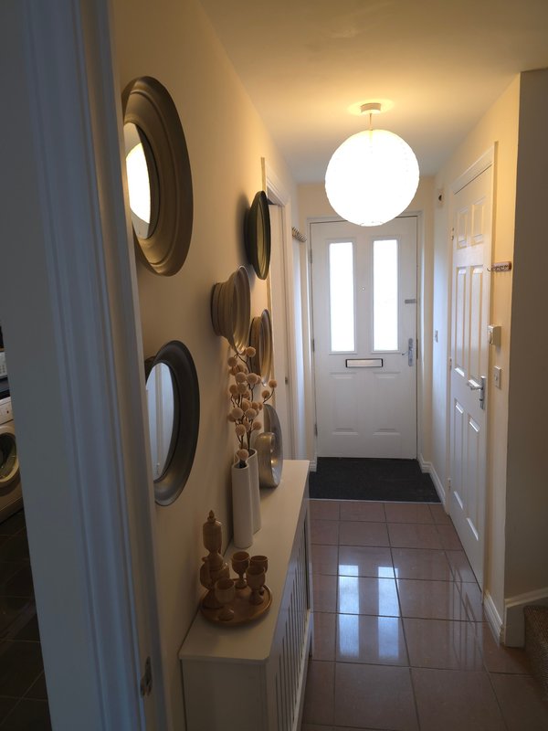 Bright hallway with circular wall mirrors, decorative items on shelf, and front door with natural light