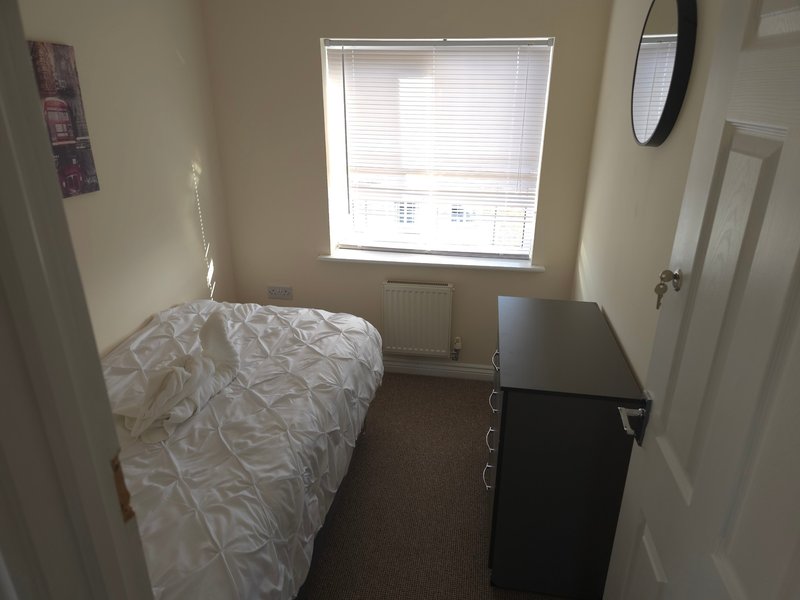 Small bedroom with single bed, desk, window with blinds, and brown carpet flooring