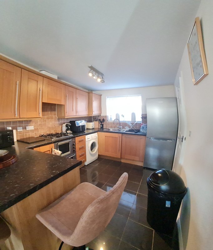 Kitchen with wooden cabinets, black countertop, stainless steel appliances and dining chair