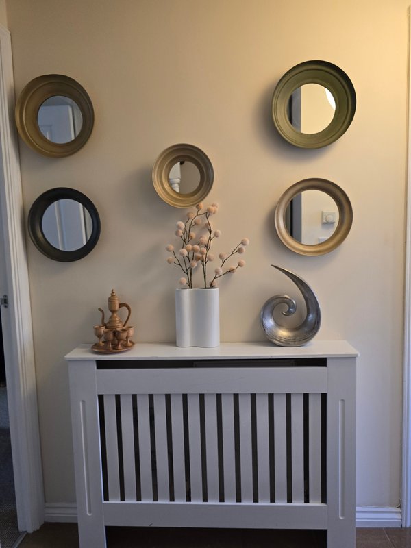 White radiator cover with decorative mirrors, vase with dried flowers, and ornaments on wall