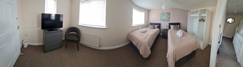 Bright bedroom with two twin beds, TV, armchair and windows overlooking garden