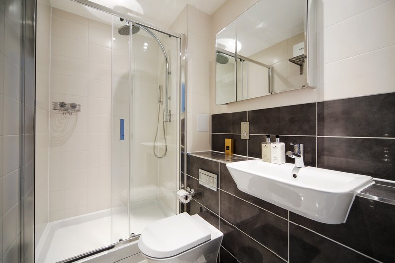 Modern bathroom with black and white tile, walk-in shower, white sink and toilet