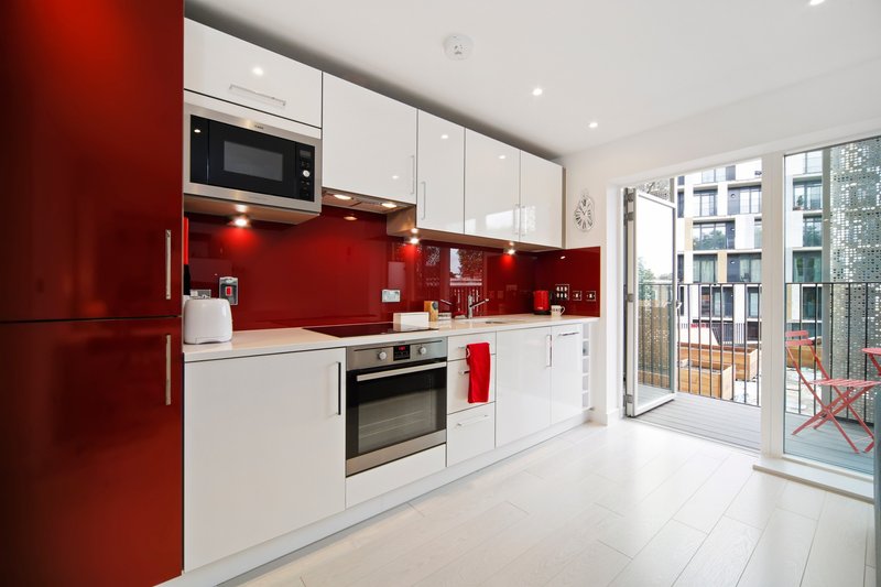 Modern kitchen with red and white cabinetry, stainless steel appliances, and glass doors to balcony