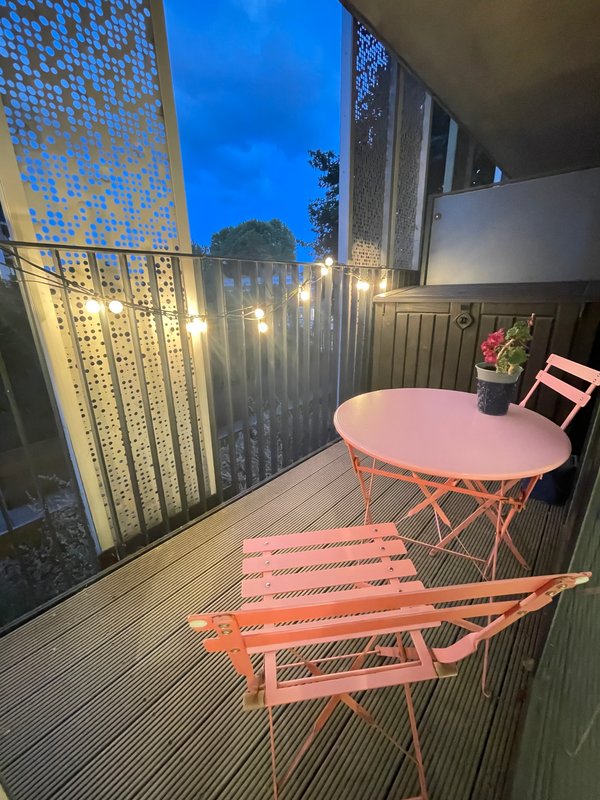Outdoor balcony with pink round table, coral lounger, and decorative screening at dusk