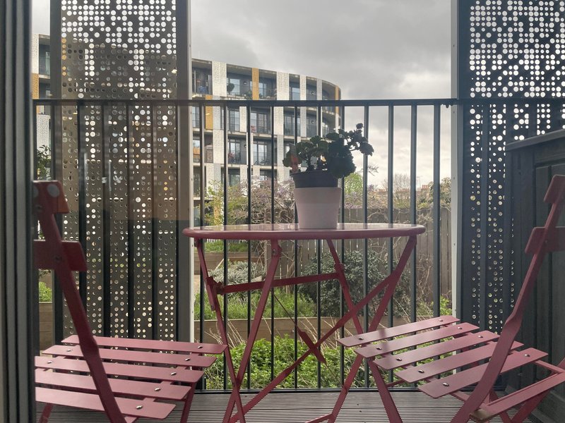 Balcony with pink wooden chairs, decorative screens, railing and potted plants overlooking garden