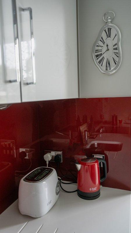 Kitchen counter with red backsplash, white appliance, red kettle, and wall clock