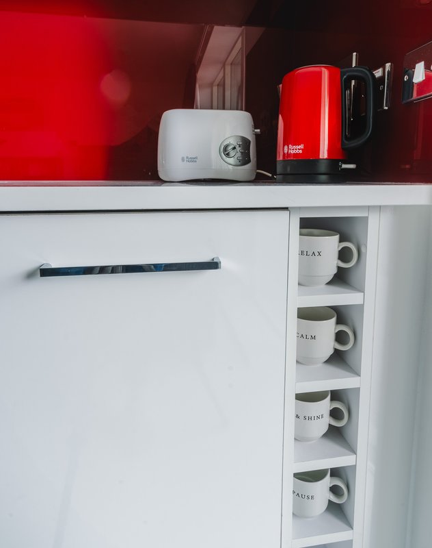 Modern kitchen counter with white cabinets, red kettle, white projector, and mug storage shelf