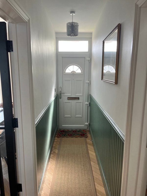 Narrow hallway with white walls, green wainscoting, pendant light and front door with fanlight