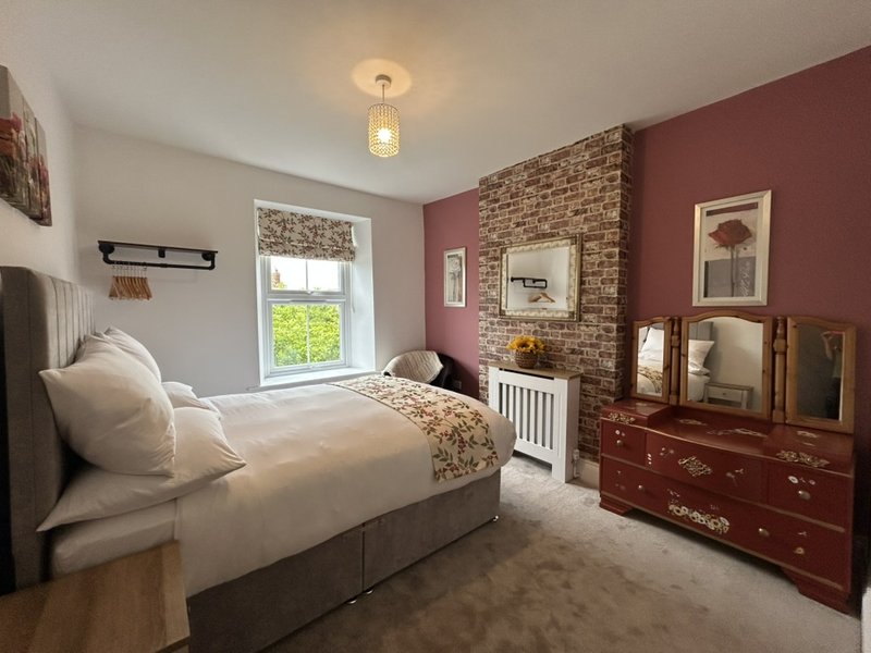 Bedroom with double bed, exposed brick wall, burgundy accent wall, wooden dresser and mirror