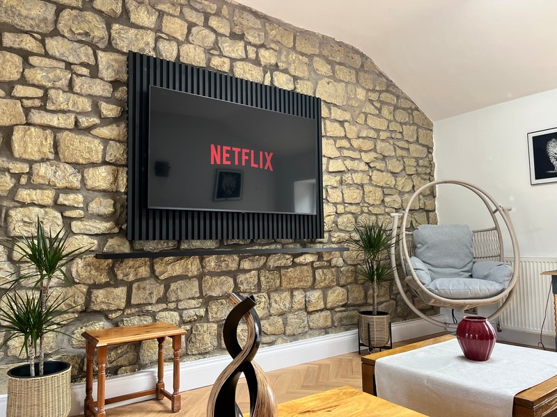 Living room with stone accent wall, wall-mounted TV, wooden furniture, and hanging chair