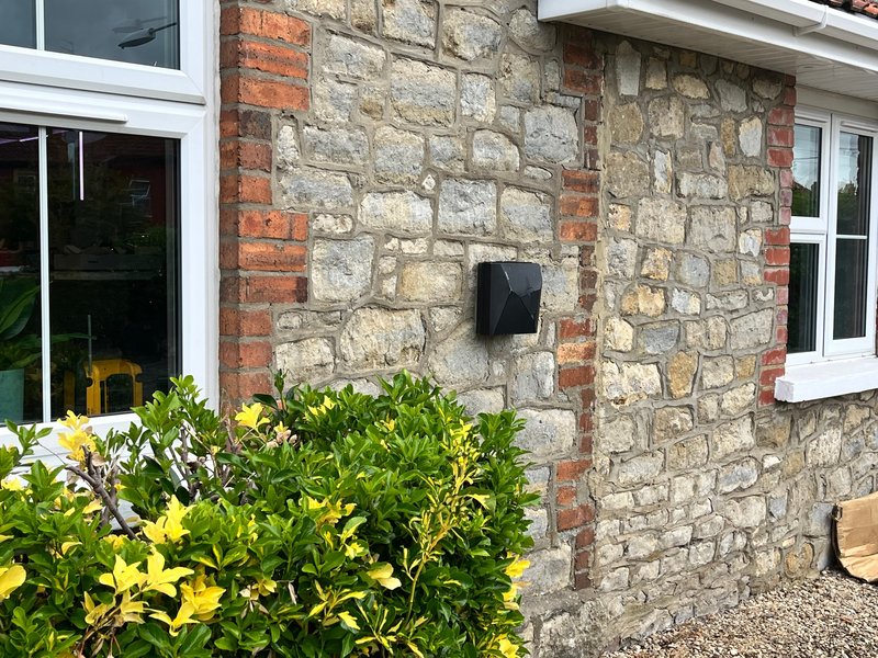 Stone and brick cottage exterior with white-framed windows, green shrubs and yellow flowers