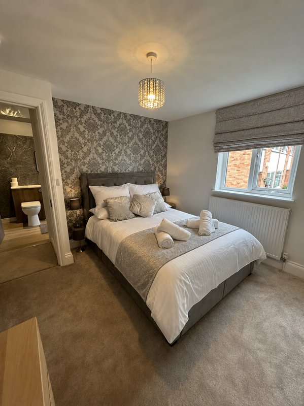 Modern bedroom with double bed, patterned headboard wall, pendant light fixture and ensuite doorway