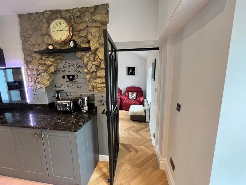 Modern kitchen with dark countertop, white cabinetry, wall clock, and open doorway to bedroom