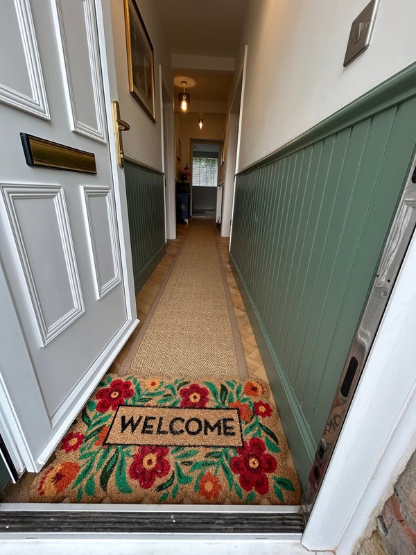 Narrow hallway with white doors, green paneling, and floral welcome mat
