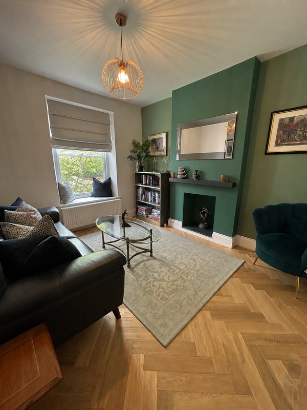 Living room with green accent wall, fireplace, black sofa, pendant light and herringbone flooring