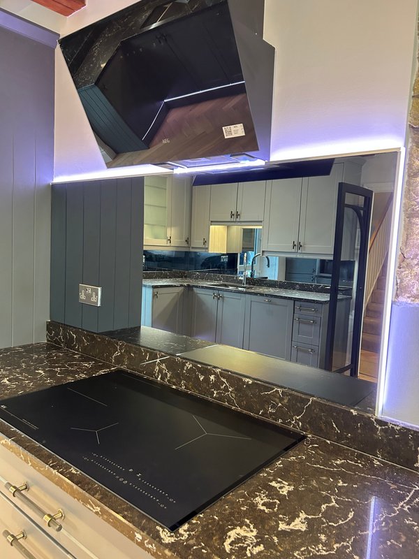 Modern kitchen with grey cabinetry, dark marble countertop, induction cooktop and ambient blue lighting