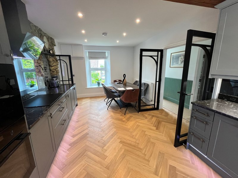 Open-plan kitchen and dining area with grey cabinetry, herringbone wood flooring, and black-framed mirrors