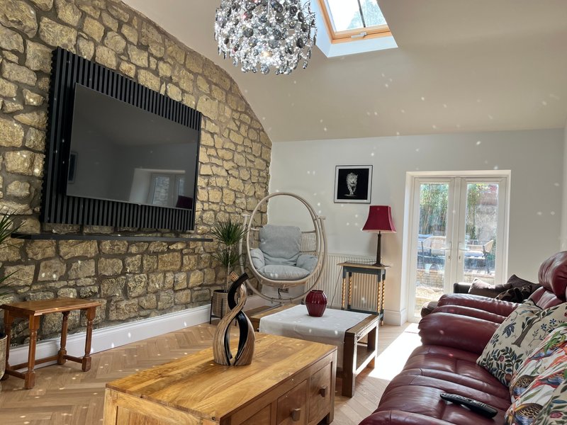Modern living room with stone fireplace, wall-mounted TV, wooden table, and burgundy leather sofa