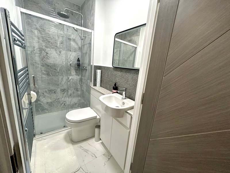 Modern bathroom with shower enclosure, white sink vanity, toilet, and mirror