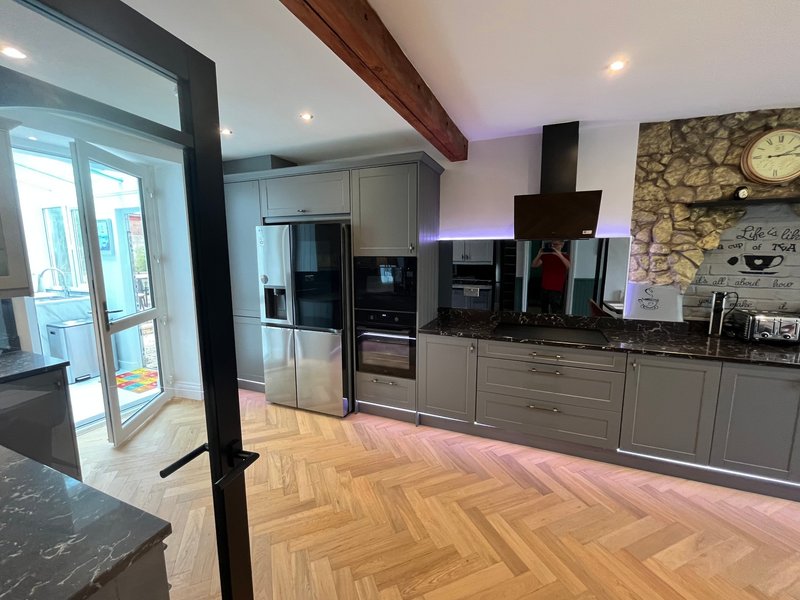 Modern kitchen with grey cabinetry, stainless steel appliances, wooden herringbone flooring and exposed beam