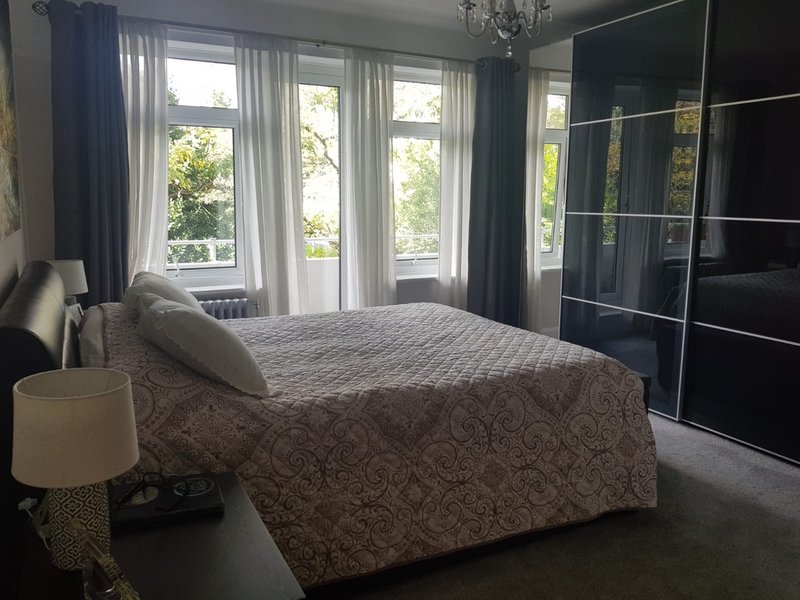 Bright bedroom with double bed, large windows, dark wardrobe and bedside lamp
