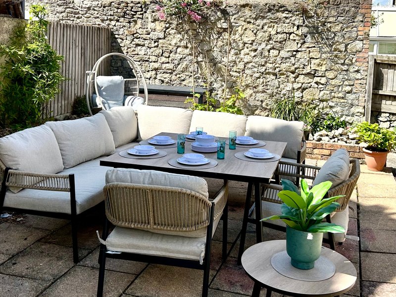 Outdoor patio with curved seating, dining table set for four, potted plants and stone wall backdrop