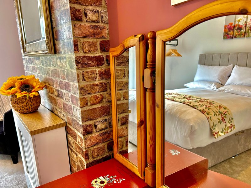 Bedroom with wooden bed frame, brick accent wall, sunflowers in basket, and red floor mat