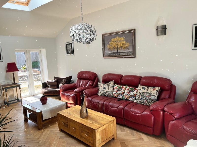 Bright living room with red leather sofas, wooden coffee tables, pendant light, and framed artwork