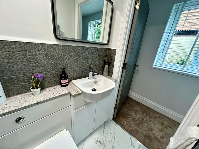 Modern bathroom with white vanity, round sink, dark tile backsplash, mirror and window